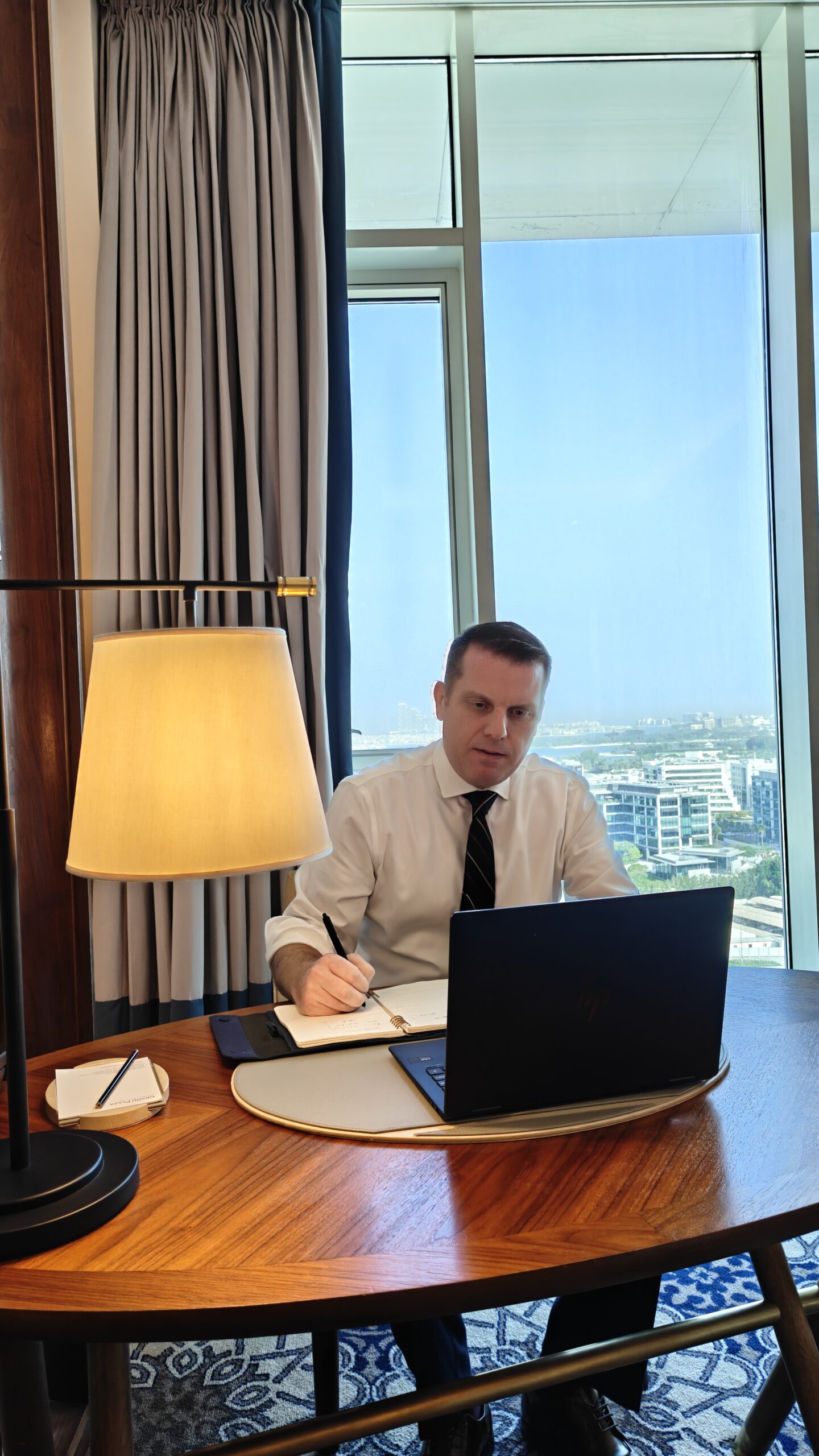 International financial adviser working at a desk with a laptop and city skyline view, reviewing client portfolio and business strategy