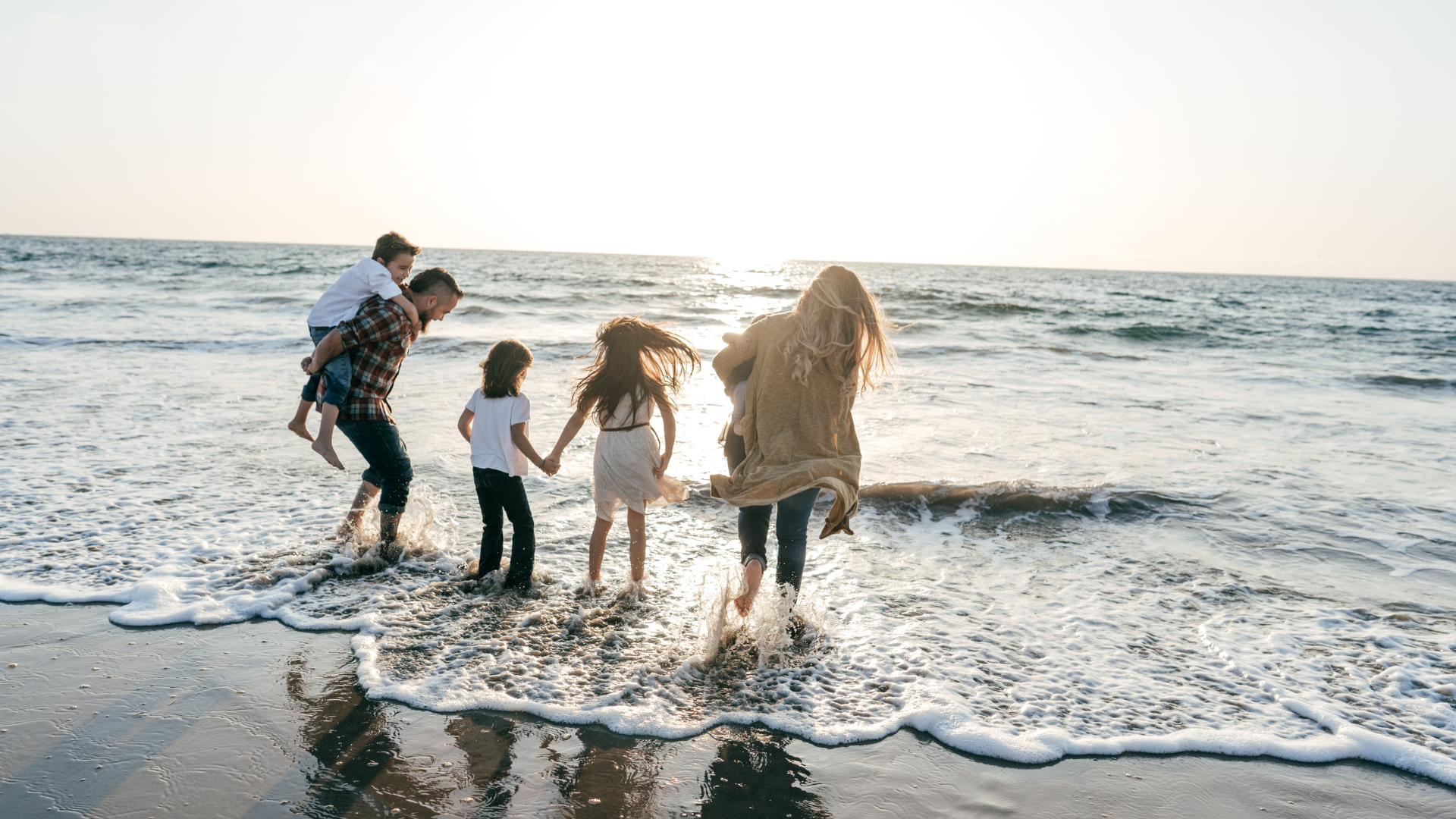 A family with young children running and playing in the shallow surf on a sandy beach at sunset, conveying the freedom and lifestyle that citizenship by investment can offer.